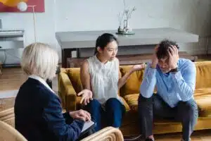 A stock photo that shows a couple on a therapy couch talking animatedly in front of a therapist.