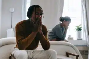 A stock photo that shows a Black man and woman sitting in a bedroom looking distressed.