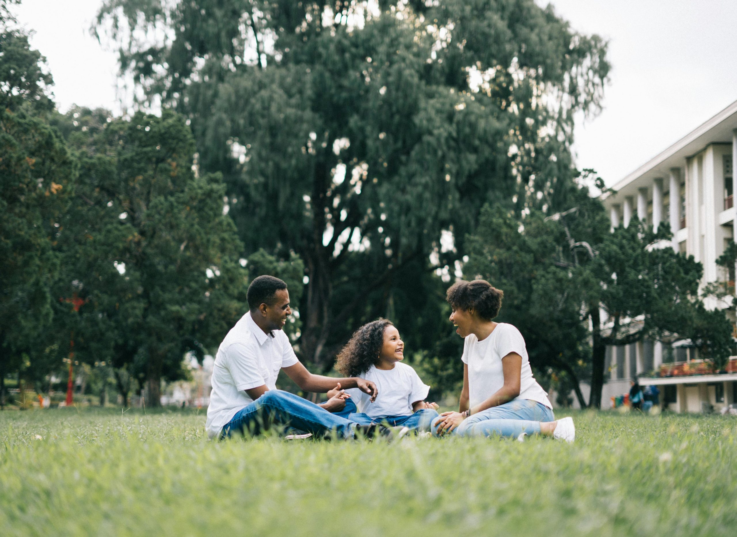 Smiling family sitting together on grass in a park, enjoying a peaceful moment outdoors.