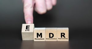 Wooden blocks spelling EMDR (Eye Movement Desensitization and Reprocessing) with a hand pointing at the first block.
