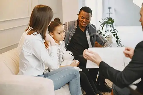 Family with young child in a counseling session, sitting together and engaging with a therapist.