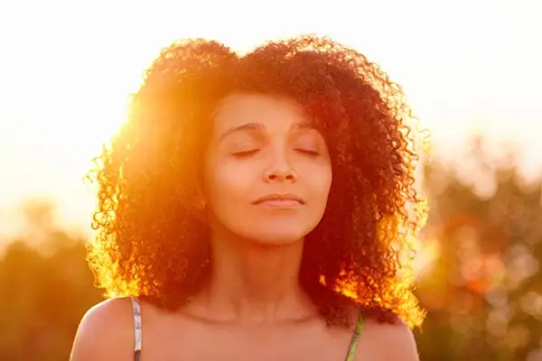 Peaceful woman with closed eyes standing in sunlight, symbolizing healing and calm after loss.