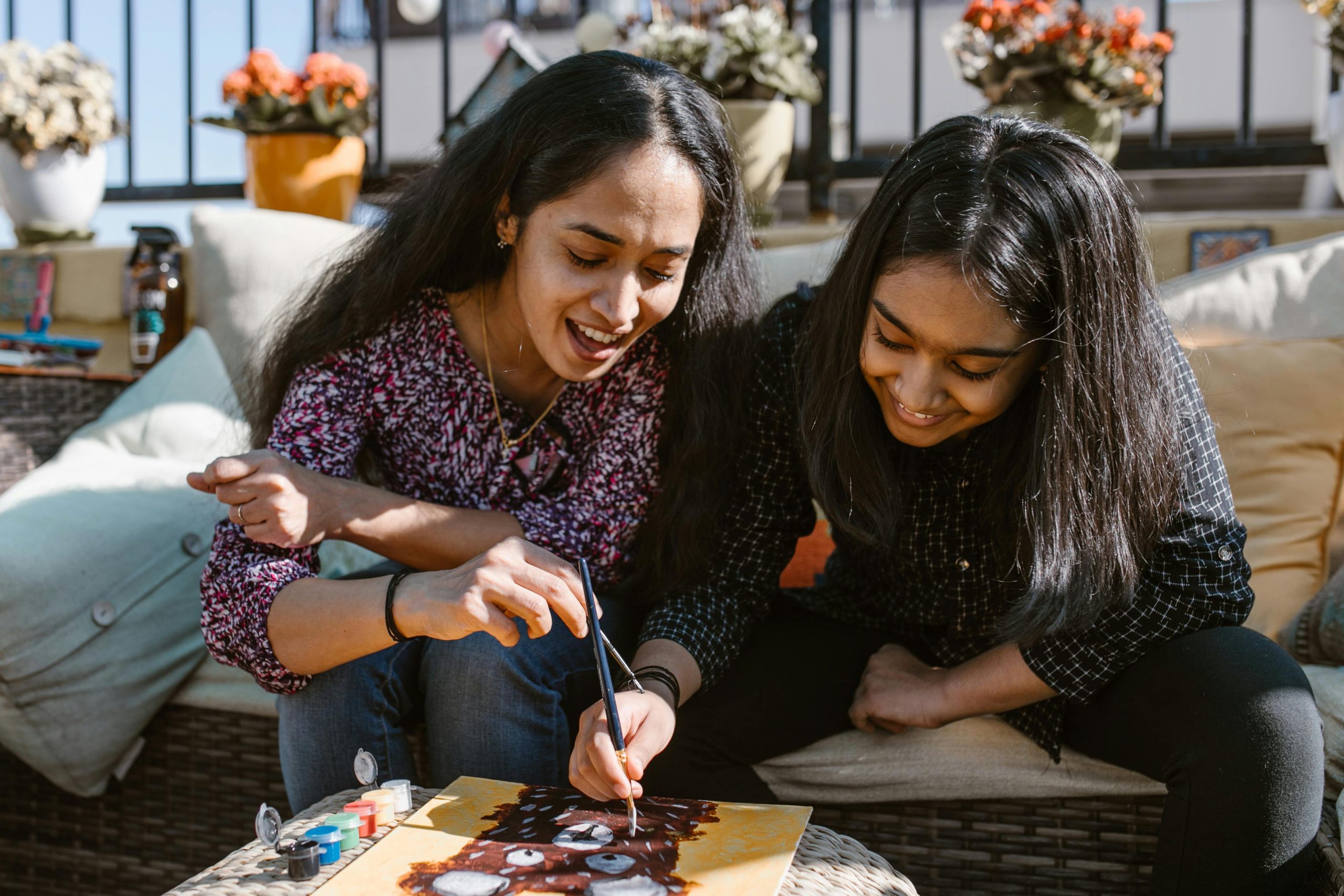 Smiling mother and teenage daughter painting together, enjoying a creative bonding activity.