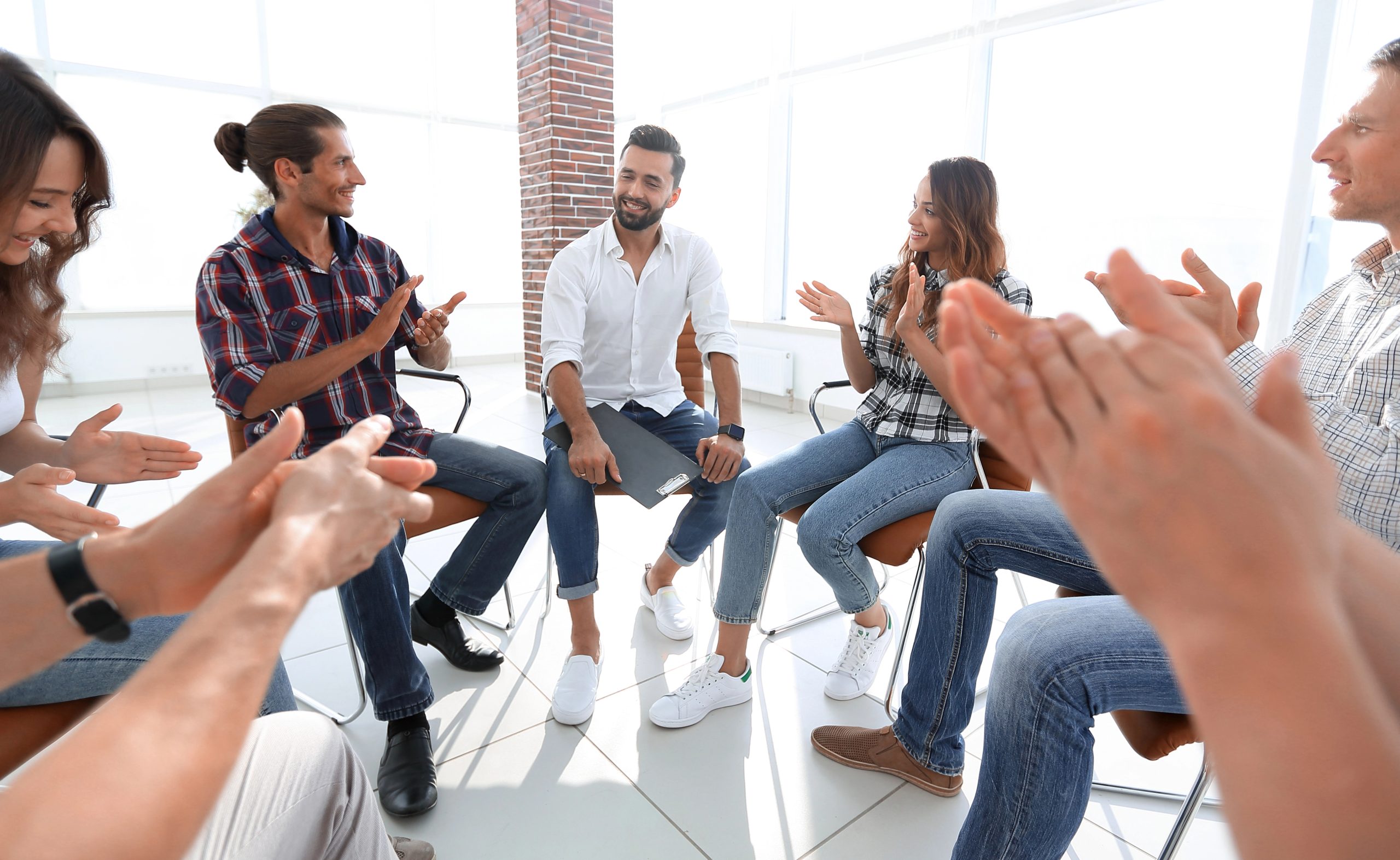 Support group sitting in a circle, clapping and encouraging one another.
