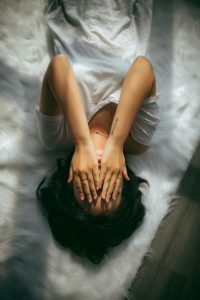 A person laying on a bed with their hands over their face.