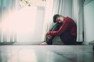 A man sitting on the floor, hugging his knees to his chest.