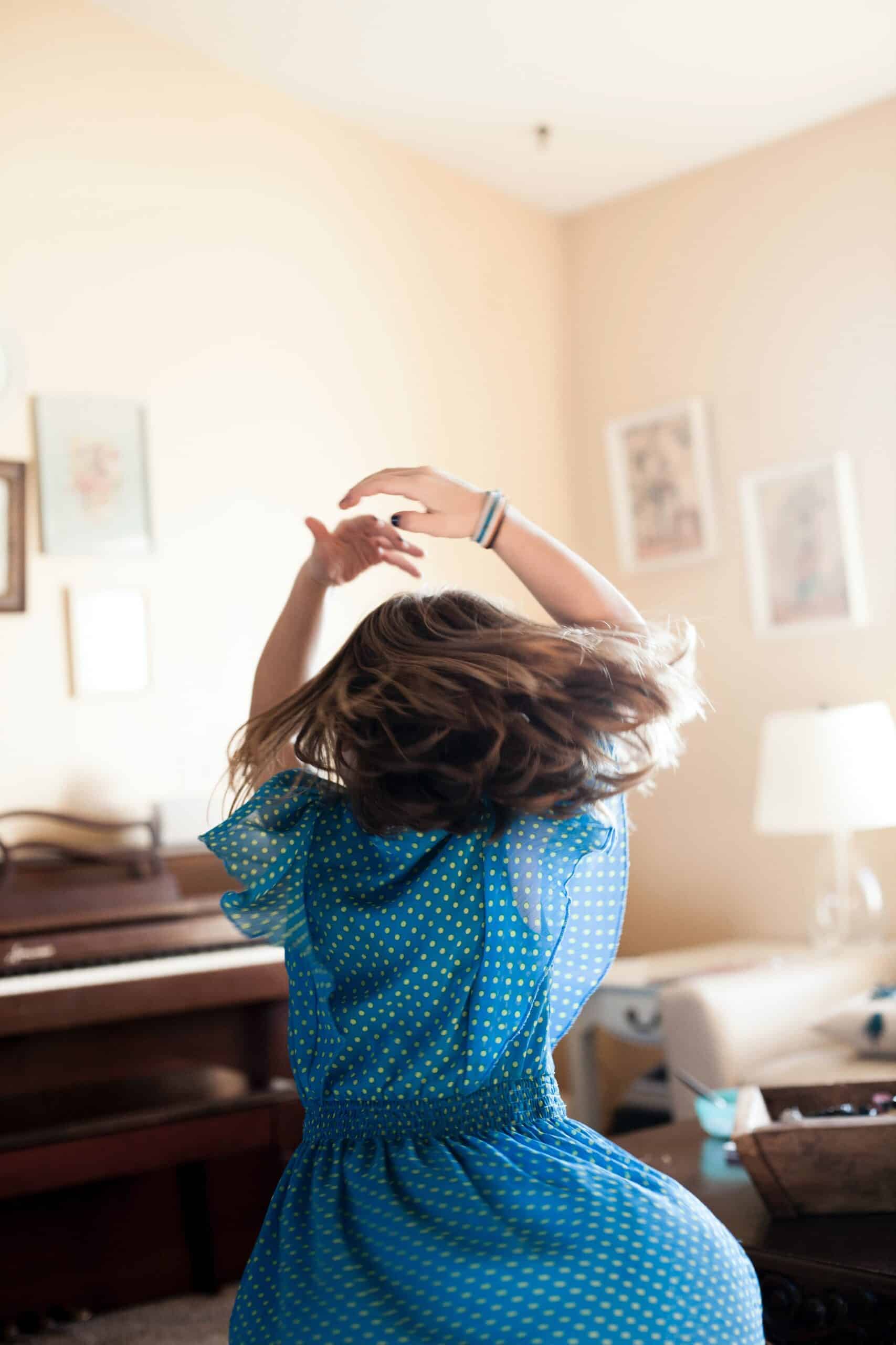 woman seen from the back with arms above her head dancing in a living room