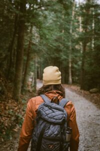 A stock photo of a man from behind, hiking in a wooded area, wearing a hat, orange coat, and backpack.