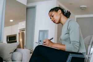 A therapist with light brown skin and her hair pulled back witting down and writing in a notebook.