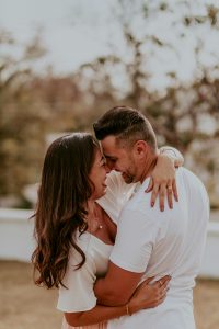 A white couple hugging and smiling at each other outdoors.
