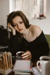 A stock photo of a teary looking white woman sitting down with her head propped on her hand, looking thoughtful.