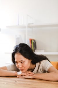 A stock photo of an Asian woman laying her head and hands on a table, with tears going down her face. 
