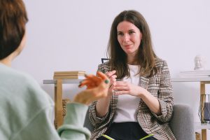 A stock photo that shows a person from behind shrugging their shoulders and talking to a white therapist, who is facing the camera. 