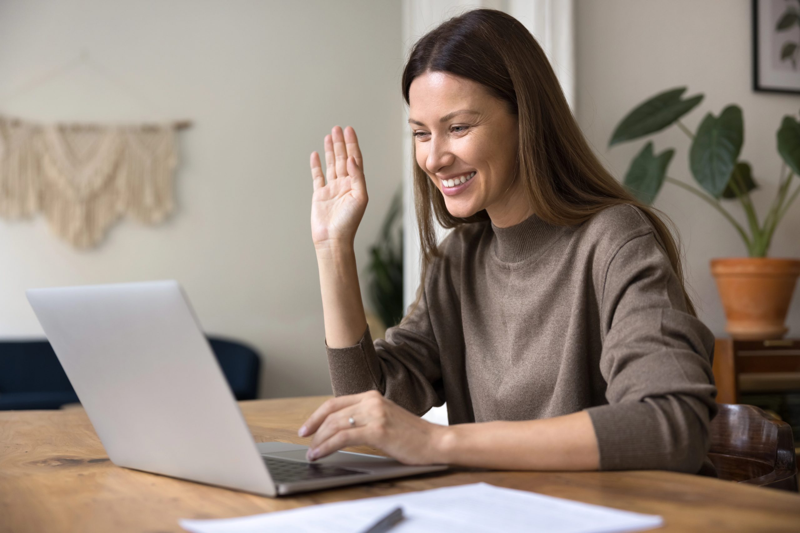 Smiling woman waving during a virtual counseling session on her laptop. 