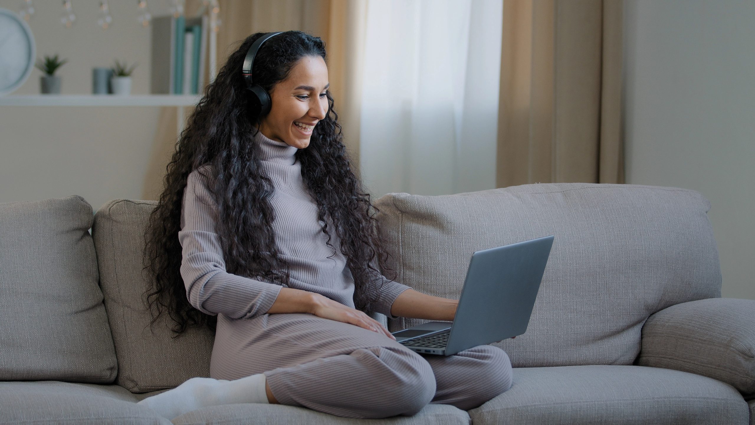 Young woman sitting on a couch, engaged in virtual therapy with headphones and a laptop.